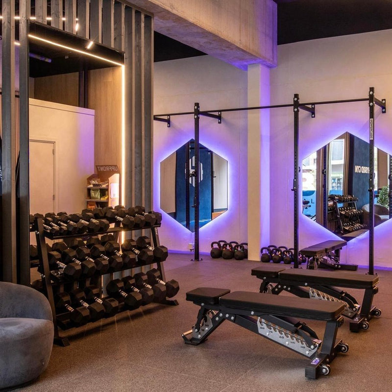 Dumbbellrek en fitnessbanken in een gym met hexagon-spiegels
